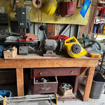 Wooden workbench area featuring power tools including a bench grinder, band saw, and leaf blower, along with various hardware accessories.