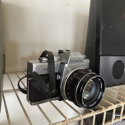 Vintage Minolta SRT101 35mm SLR camera with attached lens and leather strap, sitting on a wire shelf.