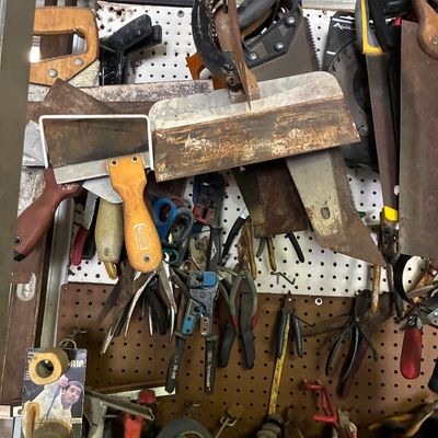 Pegboard organizer densely filled with assorted vintage hand tools, including handsaws, drywall taping knives, pliers, and wire crimpers.