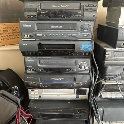Stack of vintage home electronics including VCRs, DVD players, and a time-lapse recorder from brands like Toshiba, Panasonic, Emerson,...
