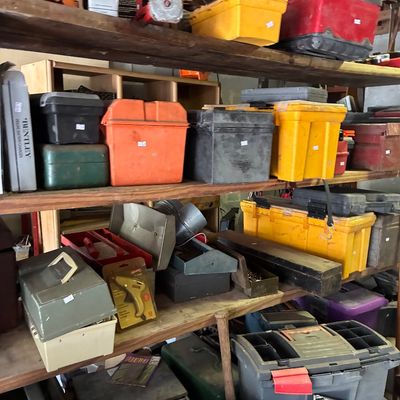 Wooden workshop shelves packed with a variety of plastic, metal, and vintage toolboxes, storage organizers, and hardware supplies.