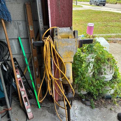 Bosch electric jackhammer breaker with attached yellow power cord, shown alongside carpenter levels in a garage doorway.