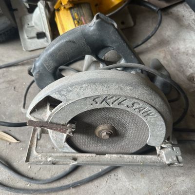 Vintage Skilsaw corded circular saw with metal housing, showing heavy surface wear and dust from use.