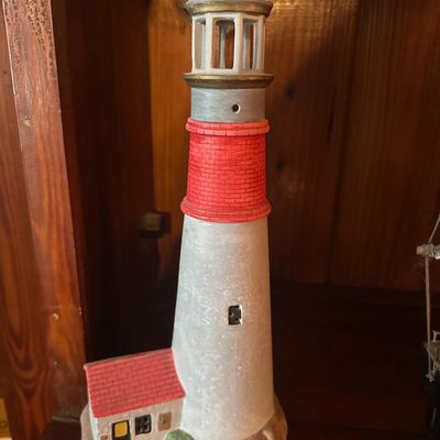 Painted ceramic lighthouse figurine featuring red brick accents and an attached keeper's cottage on a rocky base.