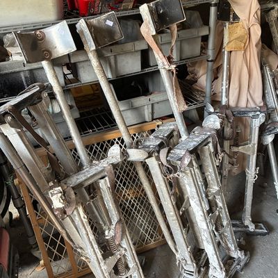 Multiple pairs of adjustable aluminum drywall stilts, showing heavy wear and drywall paste residue from practical use.