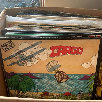 Cardboard box filled with vintage vinyl LP records, featuring Men at Work's 1983 album "Cargo" displayed at the front.