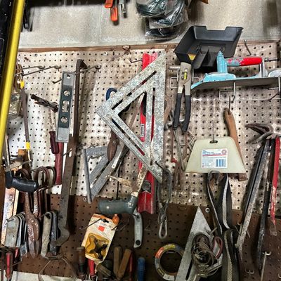 Assorted vintage hand tools and workshop equipment hanging on pegboards, including speed squares, pry bars, levels, and clamps.