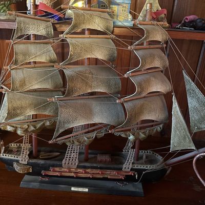 Vintage Spanish frigate model ship featuring textured metallic sails, intricate rigging, and red pennant flags mounted on a wooden base.