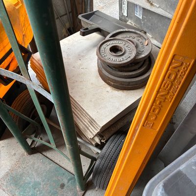 Collection of garage and hardware items, including cast iron weight plates stacked on ceramic tiles resting on a hand truck, an orange...