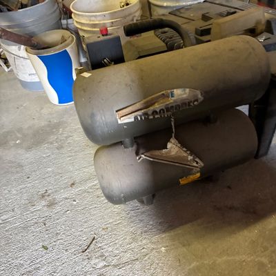 Portable twin-tank air compressor showing heavy surface dust and wear from workshop use.