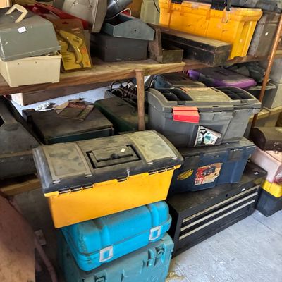 Collection of assorted plastic and metal toolboxes, power tool storage cases, and workshop supplies on wooden shelving.