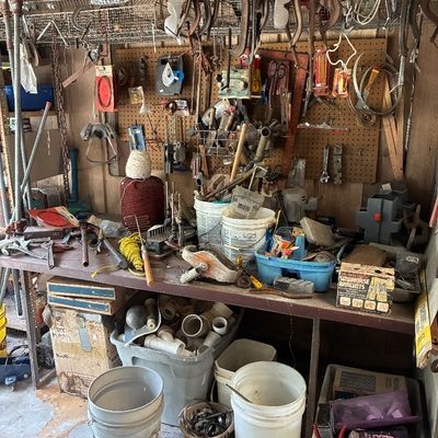 Workshop workbench area filled with vintage hand tools, clamps, buckets of PVC fittings, and various hardware.