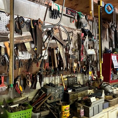 Workshop wall filled with assorted hand tools, including vintage handsaws, levels, pegboard storage, and small parts organizers.
