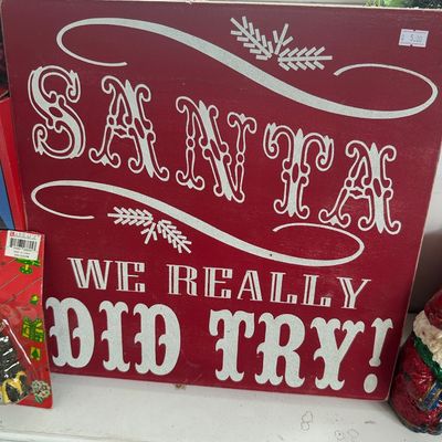 Red wooden holiday sign reading "Santa We Really Did Try!" in glittery white lettering with pine branch accents.