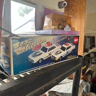 Vintage Benz Police Car 450 battery-operated toy in its original box, sitting alongside a 2004 Chevron collectible toy car.