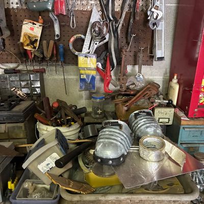 Assorted workshop tools and hardware including a pegboard wall with hand tools, pipe wrenches, plastic storage bins, and metal knee pads.