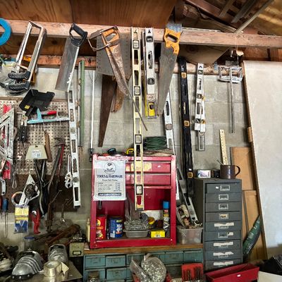 Workshop area filled with various vintage hand tools, levels, handsaws, a red tool cabinet, and small hardware organizer drawers.