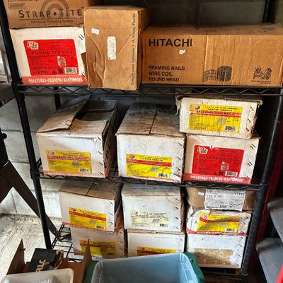 Wire wire shelf unit stacked with boxes of construction fasteners and coil nails, including brands like Hitachi and Grip-Rite.
