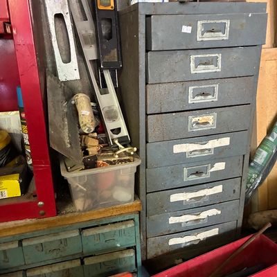 Vintage tall steel industrial drawer cabinet, showing surface rust and wear, surrounded by assorted hand tools, spirit levels, and...