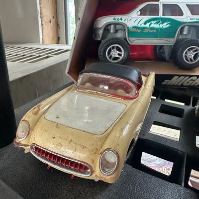 Vintage plastic Chevrolet Corvette model car with visible surface wear, shown alongside a boxed 4x4 Big Sur toy truck.