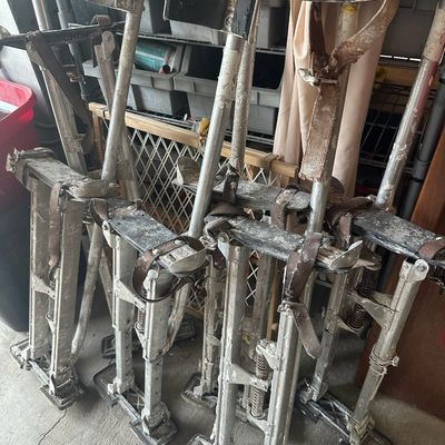 Multiple pairs of adjustable aluminum drywall stilts, heavily used with visible drywall mud and paint splatters.