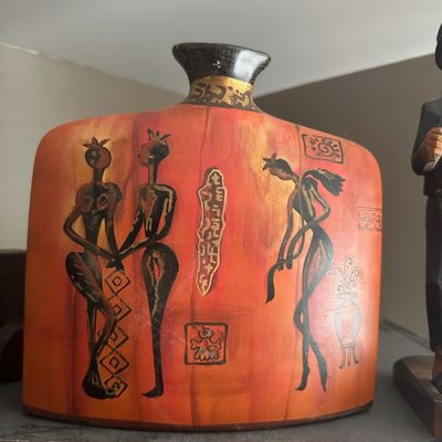 Mid-century modern decorative orange ceramic flask-style vase, featuring painted stylized figures and gold-tone geometric motifs.