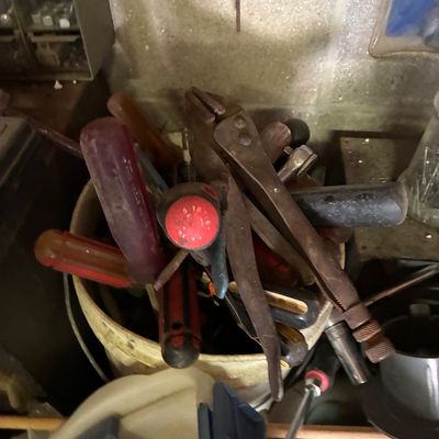 Assorted vintage hand tools stored in a bucket, including screwdrivers, pliers, and wrenches showing signs of age and heavy use.