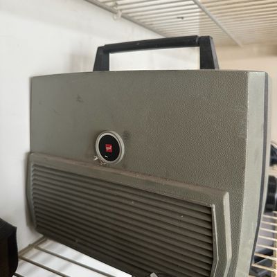 Vintage GAF slide projector in a grey carrying case sitting on a closet shelf.
