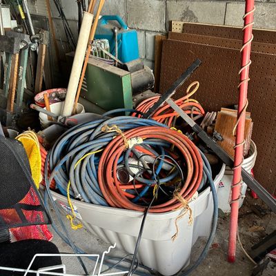 Large gray plastic storage tub filled with various coiled air hoses, extension cords, and assorted workshop supplies.
