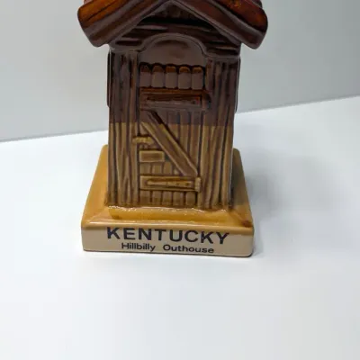 Sale Photo Thumbnail #100: The vintage "Kentucky Hillbilly Outhouse" ceramic coin bank is a popular mid-to-late 20th-century novelty travel souvenir. These campy, kitschy collectibles were mass-produced in Taiwan primarily during the 1970s and 1980s for tourist gift shops across Am