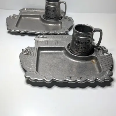 Sale Photo Thumbnail #209: The Vintage Pewter Noah's Ark Mug & Plate Set by York Metal (1977) is a classic child's dinnerware set. The divided tray measures approximately 10" x 8" shaped as the Ark, and the 3" mug often features the alphabet or Noah's Ark graphics.