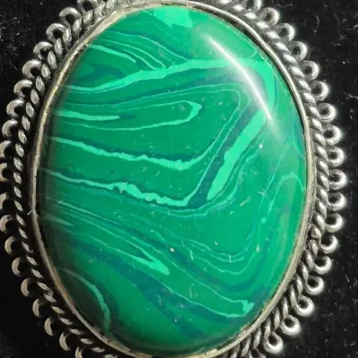 Sale Photo Thumbnail #324: Vintage filigree-style ring featuring an ornate silver mounting with scrollwork and milgrain detailing, set with a large oval green cabochon stone held by claw prongs. The band is split-shank style with decorative open metalwork on the shoulders. Pair of 