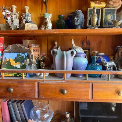 Eclectic collection of vintage decor, pottery vases, small sculptures, and hardbound books displayed on wooden hutch shelves.