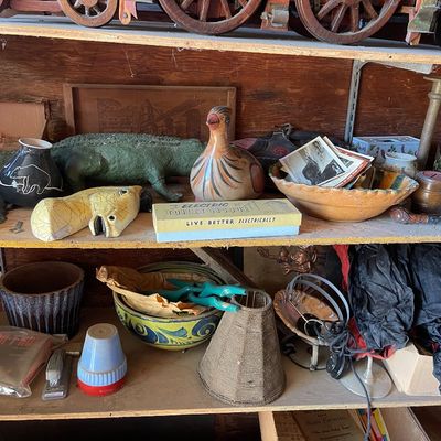 Collection of eclectic vintage decor items displayed on garage shelving, including hand-painted ceramics, a green alligator sculpture,...