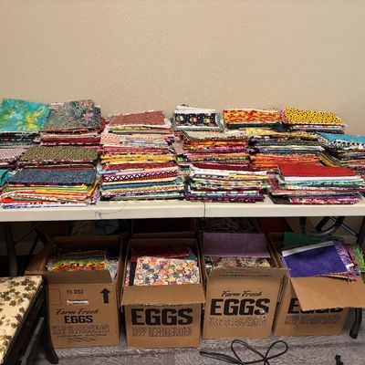 Small fabric pieces are on this table, with many boxes of small fabric underneath it and next to it.