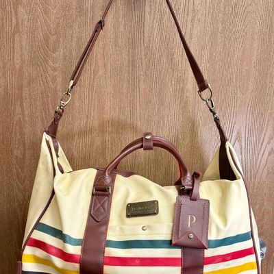 Sale Photo Thumbnail #6: Pendleton Glacier National Park canvas travel bag featuring an ivory body accented with burgundy trim and the iconic multi-color Glacier stripe pattern. Has a telescopic handle and wheels for ease of use. Like-new condition, looks to be sized for carry-on