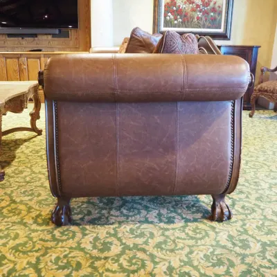 Sale Photo Thumbnail #105: Large traditional sofa upholstered in warm brown leather with oversized rolled arms, nailhead trim, carved wood base, and decorative scroll detailing. Includes coordinating oversized accent pillows and attractive aged character. 91w*38 deep* 41h