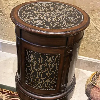 Sale Photo Thumbnail #144: Distinctive round accent table featuring a warm wood-tone case with black-and-gold ornamental inset panels and coordinating decorative top. Compact cabinet-style design with substantial Old World/Tuscan character. 22" round 28" high