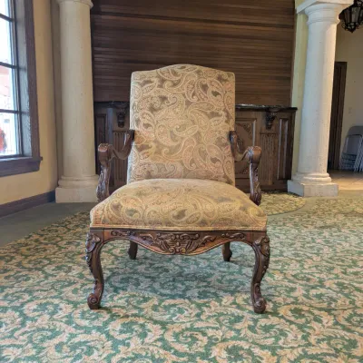 Sale Photo Thumbnail #136: High-back traditional armchair upholstered in a soft neutral paisley textile with carved wood arms, decorative apron, and cabriole-style legs. Attractive occasional chair with a more subdued palette than many of the clubhouse furnishings.