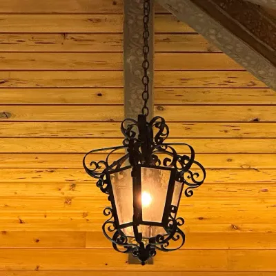 Sale Photo Thumbnail #122: Decorative hanging lantern featuring black wrought-iron-style scrollwork and warm translucent panels. Mediterranean/Tuscan styling with dramatic architectural presence. One of four coordinating fixtures available. Buyer responsible for removal.