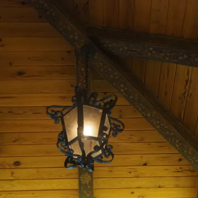 Sale Photo Thumbnail #120: Decorative hanging lantern featuring black wrought-iron-style scrollwork and warm translucent panels. Mediterranean/Tuscan styling with dramatic architectural presence. One of four coordinating fixtures available. Buyer responsible for removal.