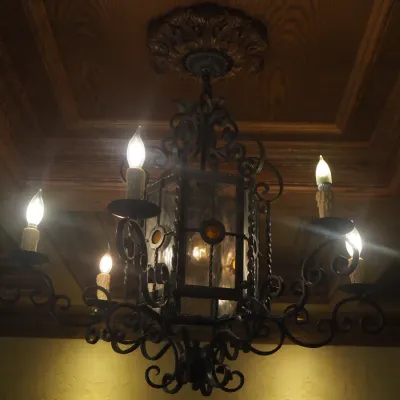 Sale Photo Thumbnail #127: Substantial Old World chandelier combining a central lantern with multiple scrolling candelabra arms. Ornate iron construction and dramatic scale make this an impressive foyer, dining, or great-room fixture. One of three coordinating fixtures available. B