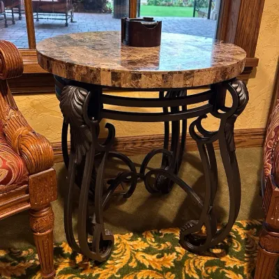 Sale Photo Thumbnail #20: Round accent table featuring a polished stone or marble-style top over an ornate black iron base with sculptural leaf and scroll detailing. A substantial decorator piece with strong Mediterranean styling. 23" round