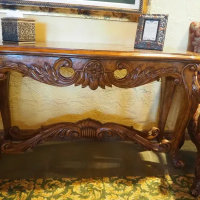 Sale Photo Thumbnail #152: Substantial traditional console table featuring extensive carved scroll and leaf detailing, shaped legs, and a decorative lower stretcher. Rich wood finish and architectural styling make this an attractive foyer, sofa, or hallway piece. 58"wx20"d*33.5h