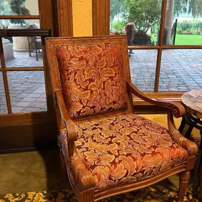 Sale Photo Thumbnail #133: Decorative traditional armchair featuring richly patterned burgundy and gold upholstery within an exposed carved wood frame. Detailed arms, fluted legs, and architectural woodwork give this chair a substantial decorator-quality appearance.  28w*30deepx42h