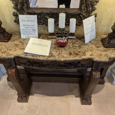 Sale Photo Thumbnail #51: Large ornate console or entry table featuring a stone or marble-style top, carved wood base, decorative drawer fronts, and substantial turned legs. Designed as a statement foyer piece and formerly used in an upscale clubhouse setting. 68"w*28"d*37"h