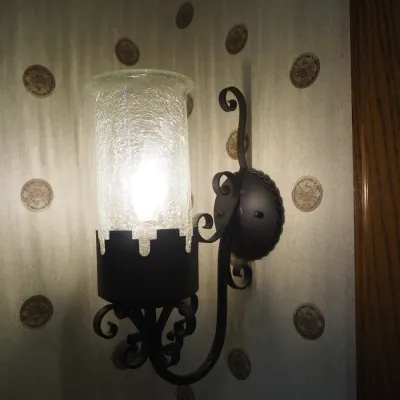 Sale Photo Thumbnail #6: Pair of traditional wall sconces featuring dark iron scrollwork and tall cylindrical crackle-glass shades. Old World styling with warm decorative light and substantial wall presence.
