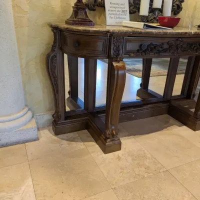 Sale Photo Thumbnail #52: Large ornate console or entry table featuring a stone or marble-style top, carved wood base, decorative drawer fronts, and substantial turned legs. Designed as a statement foyer piece and formerly used in an upscale clubhouse setting. 68"w*28"d*37"h