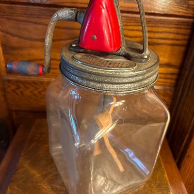 Sale Photo Thumbnail #748: This is a vintage Standard Churn Company (SCC) "Farm Master" 8-quart glass hand-crank butter churn, featuring a square jar, red-painted gear cover, and wooden paddles inside.