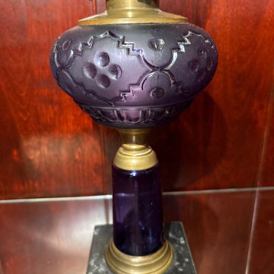 Sale Photo Thumbnail #557: antique Victorian amethyst glass and brass kerosene/oil lamp, likely dating to the late 19th century (circa 1860–1880s), featuring a patterned purple glass font, a brass connector, and a square marble base